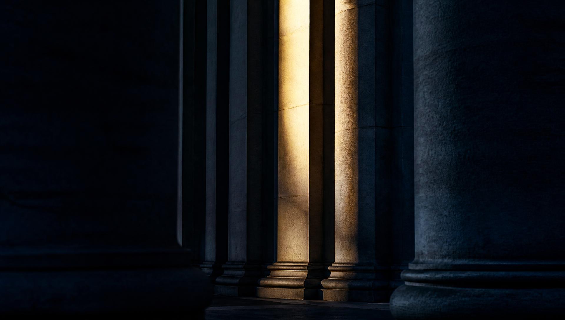 Abstract stone colonnade in shadow with a single shaft of warm light